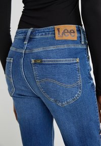 Jeans in denim blu con una vestibilità classica, cuciture gialle e un'etichetta in pelle del marchio Lee sulla vita. Presentano due tasche posteriori.