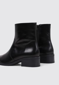 Black leather ankle boots with a smooth finish, round toe, modest heel, and a side zipper for easy wear. Simple and sleek design.