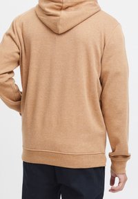 Felpa marrone con una texture morbida e vista posteriore che mette in mostra il cappuccio con cordoncino e i polsini a coste, posizionata su uno sfondo bianco uniforme.