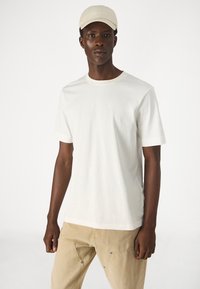 Light beige T-shirt in soft cotton with short sleeves and a rounded neckline, paired with khaki trousers featuring snap details.