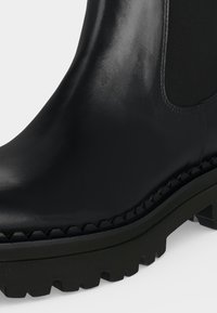 Bottine noire en cuir avec semelle épaisse et détail de panneau latéral élastique.