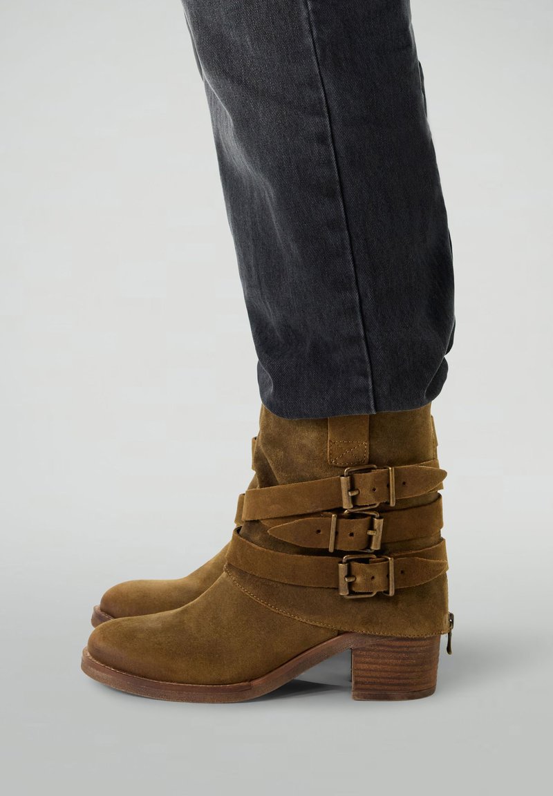 Bottines en suède marron, dotées de trois larges sangles avec boucles métalliques, d'un petit talon bloc et d'un bout arrondi. Couture renforcée.