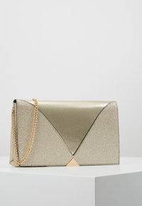 Torebka w złotym odcieniu z teksturowanym wykończeniem, trójkątnymi ozdobami i łańcuszkowym paskiem. Geometryczny design z kanciastymi kształtami i smukłymi liniami.