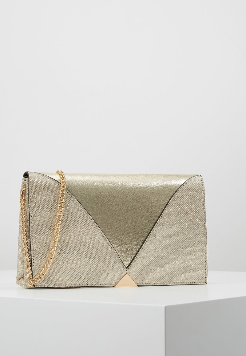 Torebka w złotym odcieniu z teksturowanym wykończeniem, trójkątnymi ozdobami i łańcuszkowym paskiem. Geometryczny design z kanciastymi kształtami i smukłymi liniami.