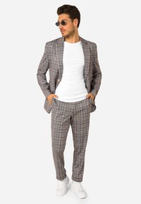 Traje de cuadros gris claro para hombre con un diseño ajustado, que incluye una chaqueta y pantalones a juego, combinados con una camiseta blanca y deportivas blancas.