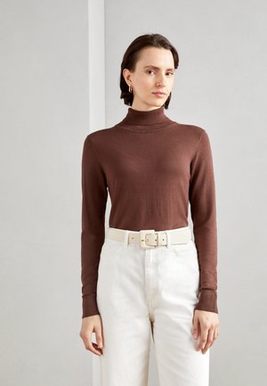 Brown turtleneck sweater paired with high-waisted white trousers. The outfit features a light-colored belt with a square buckle detail.