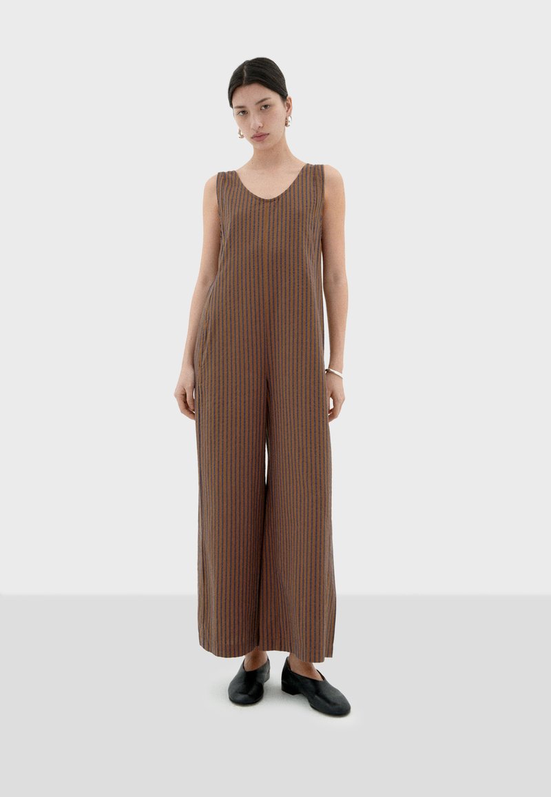 Bruine mouwloze jumpsuit met verticale blauwe strepen, wijde pijpen, een ronde halslijn en lichtgewicht stof. Draag met zwarte schoenen.