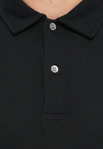 Musternükkega must polo-särk, millel on klassikaline krae ja kaks hõbedast nuppu kaelusel.