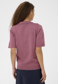 Polo w krótkim rękawie w kolorze przykurzonego różu, wykonany z dzianiny z prążkowanym wykończeniem; posiada klasyczny kołnierzyk i gładką fakturę.