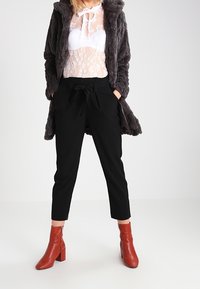 Grijze nep bontjas, doorschijnend witte kanttop, zwarte tapse broek, rode enkellaarzen met brede hakken. Opvallende texturen en contrasten.