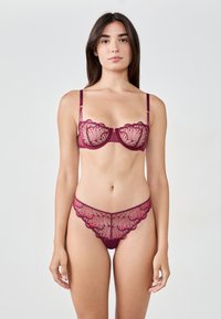 Ensemble de lingerie en dentelle bordeaux comprenant un soutien-gorge transparent avec des bords festonnés et une broderie florale, associé à des culottes en dentelle assorties.