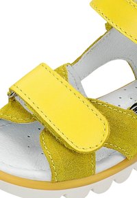 Sandali in suede giallo con cinturini in Velcro, plantare bianco imbottito e suola in gomma testurizzata. Design aperto con dettagli ritagliati.