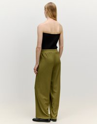 Zwarte geribbelde strapless top in combinatie met olijfgroene wijde broek. Glad oppervlak met een elastische tailleband, platte zwarte schoenen.