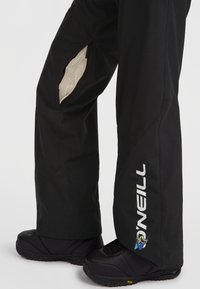 Los pantalones de nieve negros cuentan con un ajuste holgado, aberturas de ventilación forradas de malla y un logo blanco de O'Neill a lo largo de la pierna. Se combinan con botas negras.