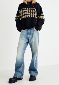 Sweat-shirt à carreaux noir et beige avec un col, associé à un jean large délavé clair et des bottes épaisses noires.