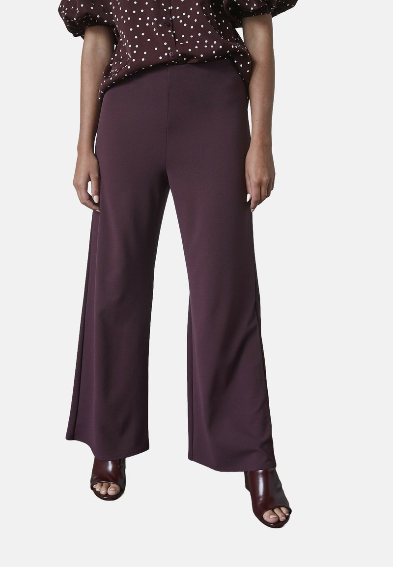 Mörklila vida byxor i ett glatt tyg, kompletterade med en mönstrad blus. Har hög midja och avslappnad passform.
