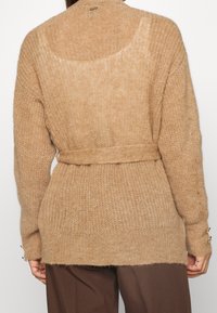 Cardigan de punto beige con un corte holgado, cintura ceñida con cinturón y mangas largas. Presenta una textura suave y peluda y botones en los puños de las mangas.