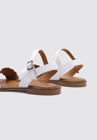 Sandalias de cuero blanco con punta abierta, tiras en el tobillo y hebillas, plantillas acolchadas marrones y suelas planas de madera.