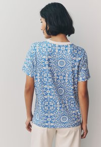 Baumwoll-T-Shirt mit blauem Hintergrund und weißem Blumenmuster, kurzen Ärmeln und rundem Halsausschnitt. Lässige Passform mit glatter Textur.