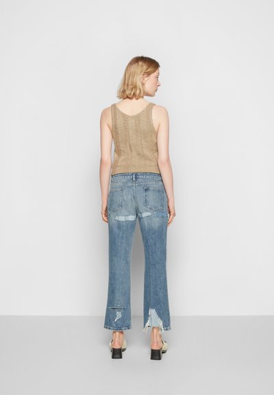 Top de malha dourado com alças largas, combinado com jeans de cintura alta e boca de sino em azul claro, apresentando bordas desfiadas e detalhes desgastados.