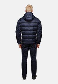 Navy puffer jacket with a hood, featuring horizontal quilted design and smooth texture. Worn with dark jeans and black shoes.