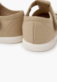 Beige kangasest libisemisega jalanõud, millel on tekstuuriga pind, valge kummist tald ja konksuga konts mugavaks selga panemiseks. Tagantvaade.