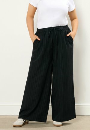 Pantaloni neri a gamba larga con un motivo a righe verticali testurizzate, vita elastica, cordoncino e tasche laterali. Abbinate a sneakers bianche.