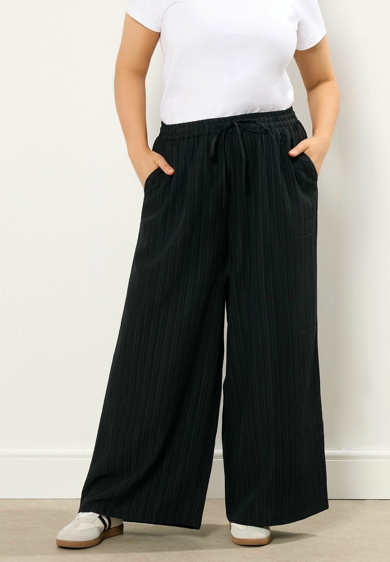 Pantaloni neri a gamba larga con un motivo a righe verticali testurizzate, vita elastica, cordoncino e tasche laterali. Abbinate a sneakers bianche.
