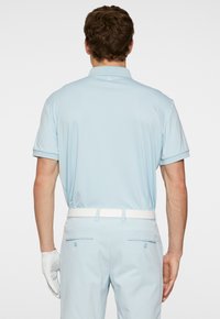 Ljusblå kortärmad polo med en strukturerad yta, med vit krage och logotyp på ryggen, parat med matchande ljusblå byxor.