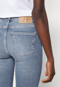 Hubené modré džínové kalhoty se světlým umytím, se značkou z kůže s nápisem "/F" a dvěma zadními kapsami s žlutým prošitím.