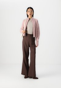 Cárdigan corto y peludo de color rosa, top de canalé beige, pantalones de pierna ancha marrones de cintura alta y zapatos de tacón marrones, con un bolso blanco.