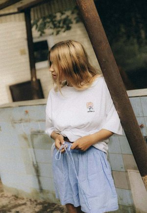 Biała, oversize'owa koszulka z nadrukiem, zestawiona z jasnoniebieskimi szortami z elastycznym pasem i sznurkiem do regulacji.