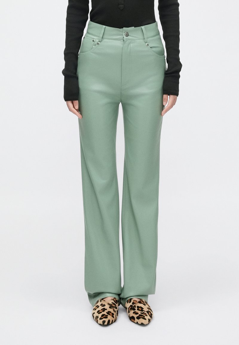 Mėtų žalsvi platūs kelnių stiliai, pagaminti iš lygaus audinio, su aukštu liemeniu ir priekinėmis kišenėmis, derinami su leopardų raštu paslystančiais bateliais.