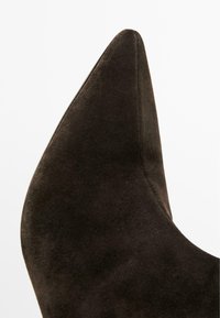 Scarpa alta in suede marrone scuro con punta affusolata e texture liscia. Presenta un design elegante con una silhouette leggermente curva.