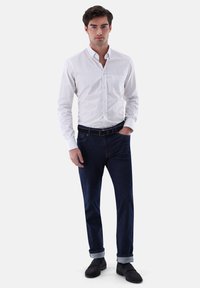 Weiß-blau gestreifte Hemd mit Knöpfen und einer Brusttasche, kombiniert mit dunklen Jeans, an den Knöcheln umgeschlagen, und schwarzen Schuhen.