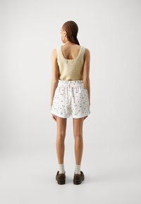 Débardeur tricoté en beige clair avec des bords festonnés, associé à un short blanc avec des motifs floraux bleus et une taille à cordon. Chaussures marron.