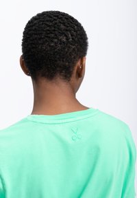 T-shirt verde menta in cotone, con collo rotondo e un piccolo emblema a forma di forbice ricamato vicino al collo sul retro.