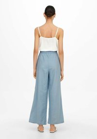 Ljusblå, vida byxor med elastisk midja, i kombination med en vit ärmlös topp. Tyget verkar slätt och lätt.