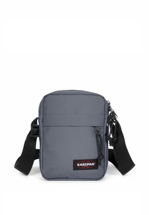 Borsa a tracolla in tessuto grigia di forma rettangolare, con tasca frontale con zip, tracolla regolabile e patch con logo.