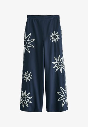 Meresinised laia lõikega püksid elastse vöökohtadega, mille eesosas on suur valge päikesekiire tikand ning külgedel kirjuga triibud.