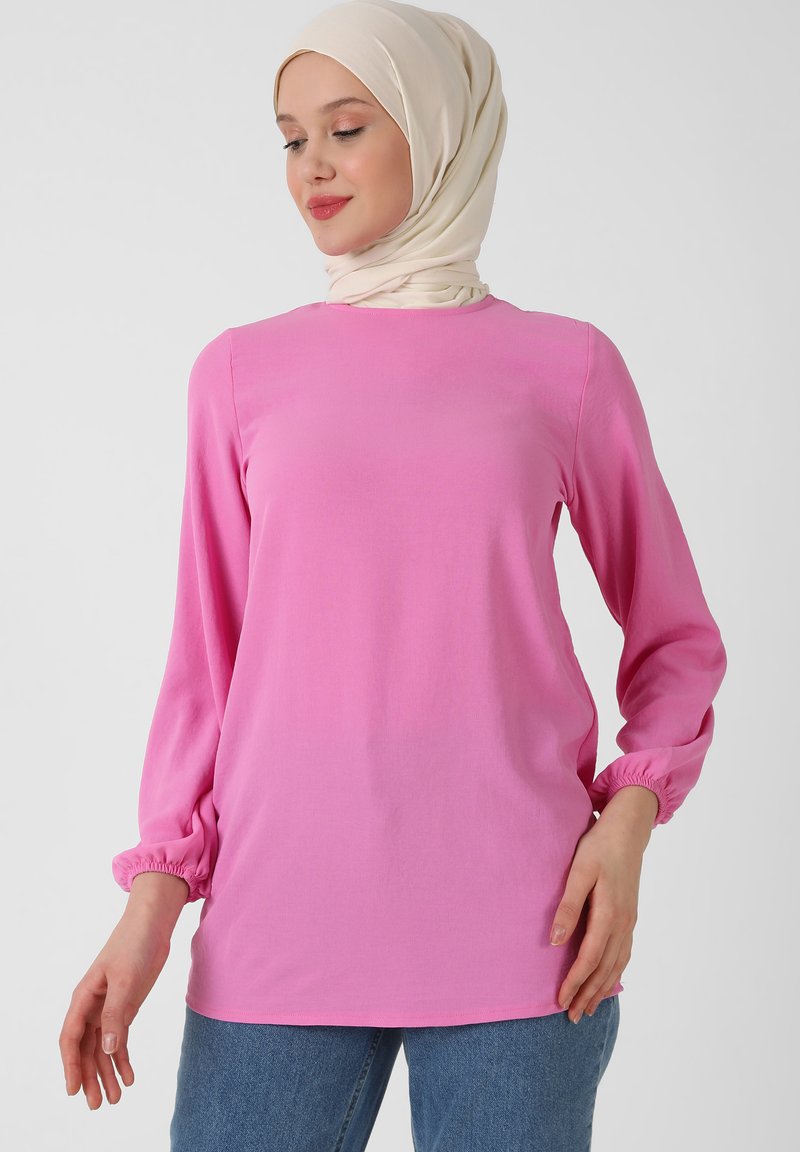 Top rosa a maniche lunghe con scollo rotondo, polsini elasticizzati e vestibilità comoda. Il tessuto appare liscio, con un design a tinta unita. Abbinato a jeans blu.