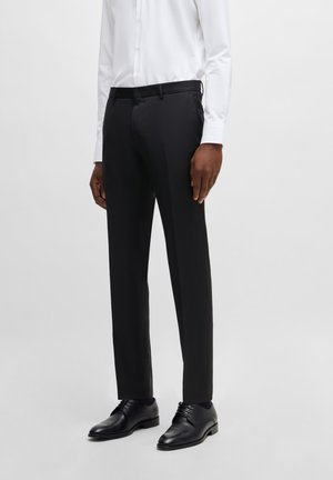 Black tailored trousers with a flat front, smooth texture, belt loops, and a slim fit, paired with black leather shoes and a white shirt.