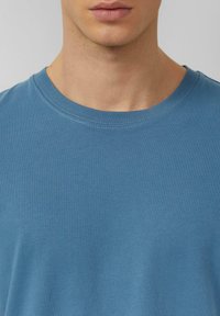 Blaues Baumwoll-T-Shirt mit rundem Ausschnitt und kurzen Ärmeln, das eine glatte Textur und eine lockere Passform aufweist. Minimale Nahtdetails am Halsausschnitt.
