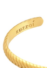 Aukso atspalvio apyrankė su pasukta forma, turinti lygią vidinę pusę, ant kurios išgraviruotas žodis "Kuzzoí".