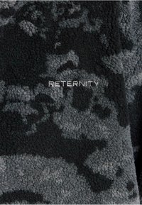 Tessuto in pile nero e grigio con un pattern marmorizzato; presenta la parola "RETERNITY" in lettere bianche. Superficie morbida e testurizzata.