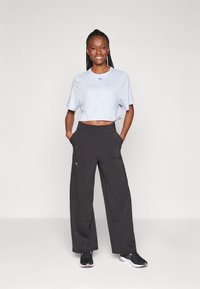 Lichtblauw cropped t-shirt met korte mouwen en een klein logo, gecombineerd met zwarte wijde broek met zijzakken en een elastische tailleband.