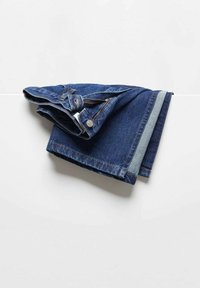 Jean en denim bleu plié avec fermeture éclair visible, bouton et passants de ceinture placés sur une surface plane blanche.