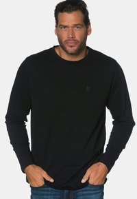 Zwarte lange mouwen shirt van zacht materiaal, met een ronde hals en een subtiele 'JP' logo op de borst, gecombineerd met blauwe jeans.