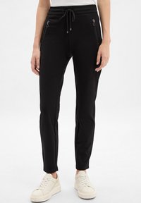 Schwarze Jogginghosen aus weichem Material, mit passgenauer Passform, verstellbarem Bund und Taschen mit Reißverschluss an den Seiten.