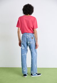 Camiseta de algodón roja combinada con jeans de mezclilla azul claro con estampados gráficos blancos. Zapatillas negras y blancas completan el conjunto.